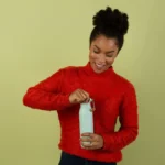 Woman smiling while opening a reusable water bottle filled with crisp, clean water filtered by the Everydrop Filter 2 system.